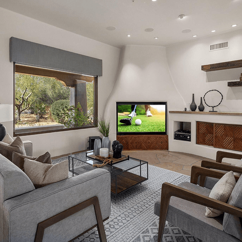 Stylish living room with a golf scene on a TV, a large window revealing a desert view, and comfortable grey seating.