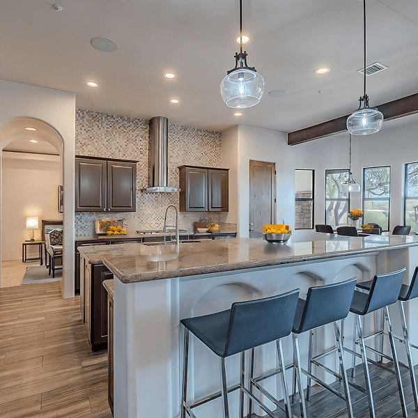 A spacious modern kitchen featuring a large granite island with bar stools, dark wood cabinets, a mosaic tile backsplash, and views through windows.