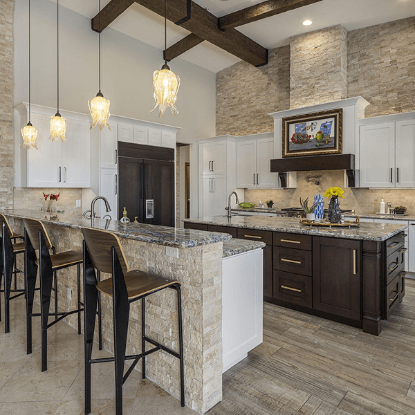 Spacious, modern kitchen featuring two islands, white and dark cabinetry, stone accent walls, vaulted ceilings with wood beams, and decorative pendant lights.