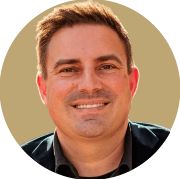 Smiling man with short dark hair wearing a black suit jacket and white collared shirt.