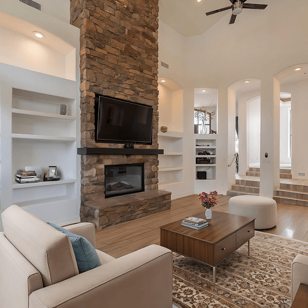 Spacious living room featuring a tall stone fireplace with a mounted TV, built-in shelves, and modern furnishings including a sofa and coffee table.